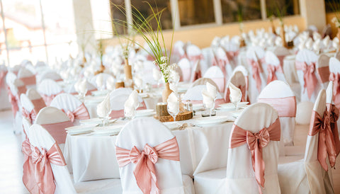 Salle de réception élégante avec housses de chaises blanches et nœuds rose poudré - décoration de table raffinée pour mariage